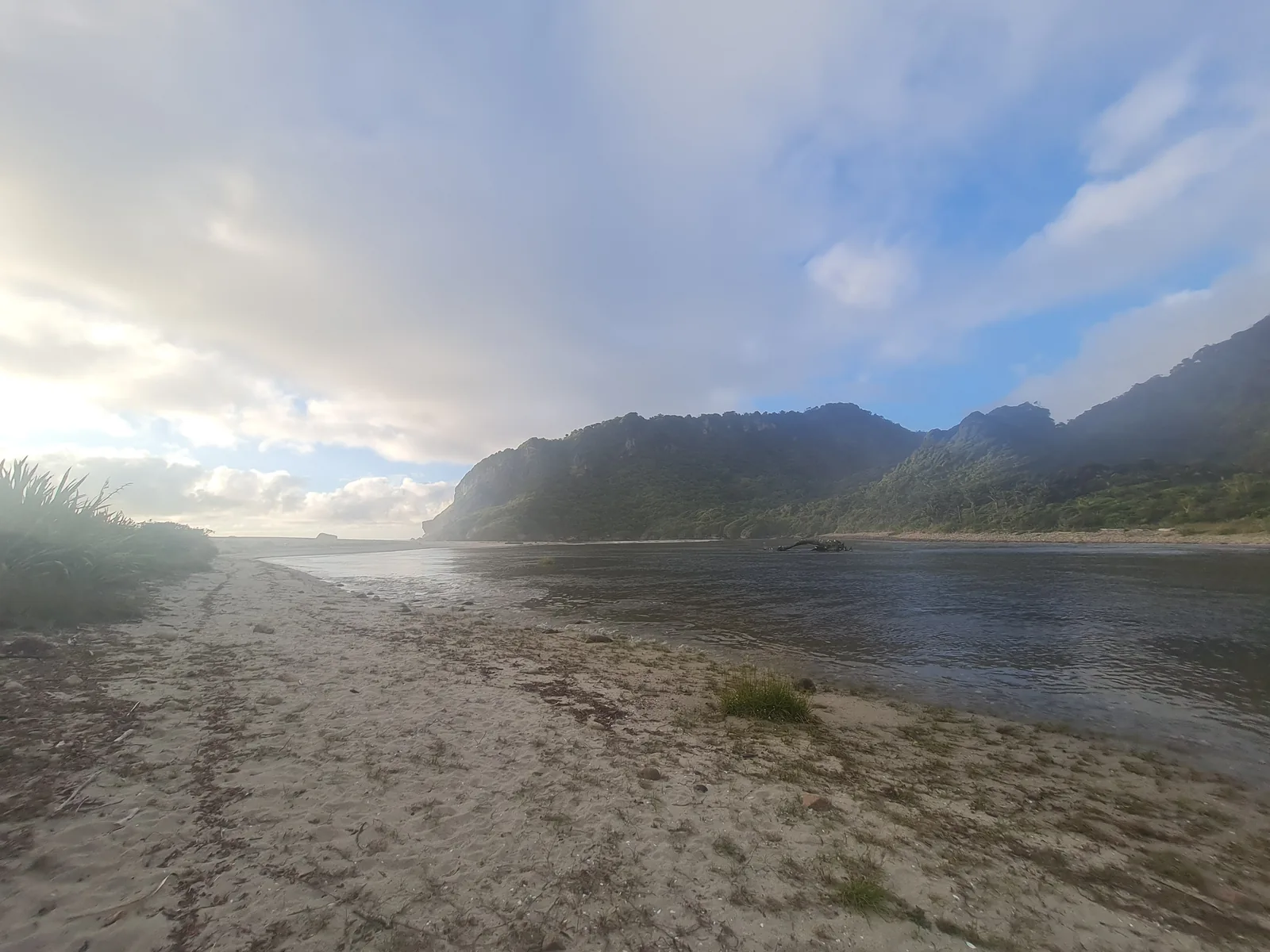 The calm, tannin-stained mouth of the Heaphy River widening into the tidal lagoon before meeting the Tasman Sea, framed by steep forested bluffs.
