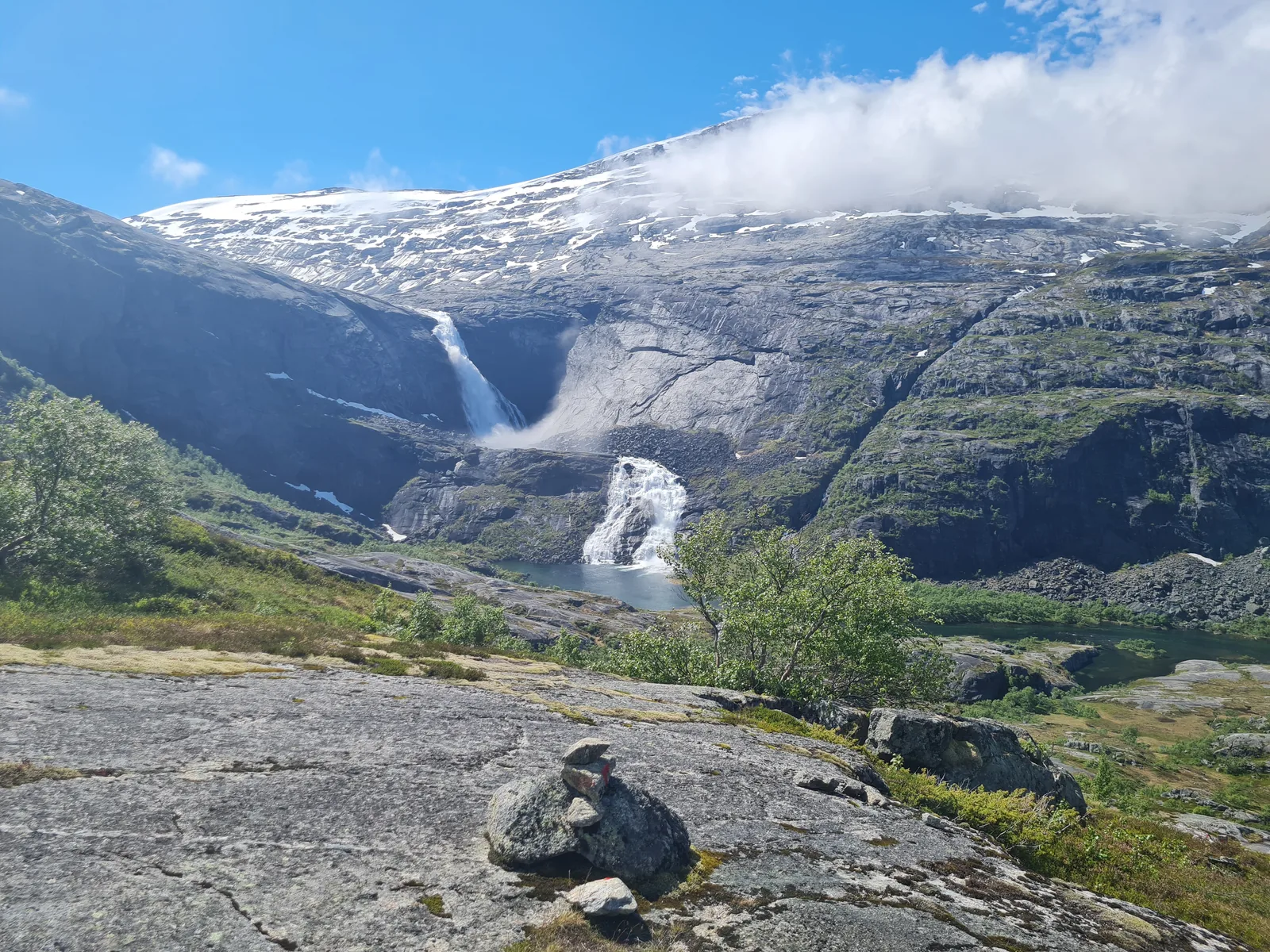 Traditional red-T stone cairn trail marker on granite bedrock facing the two tiers of Søtefossen.