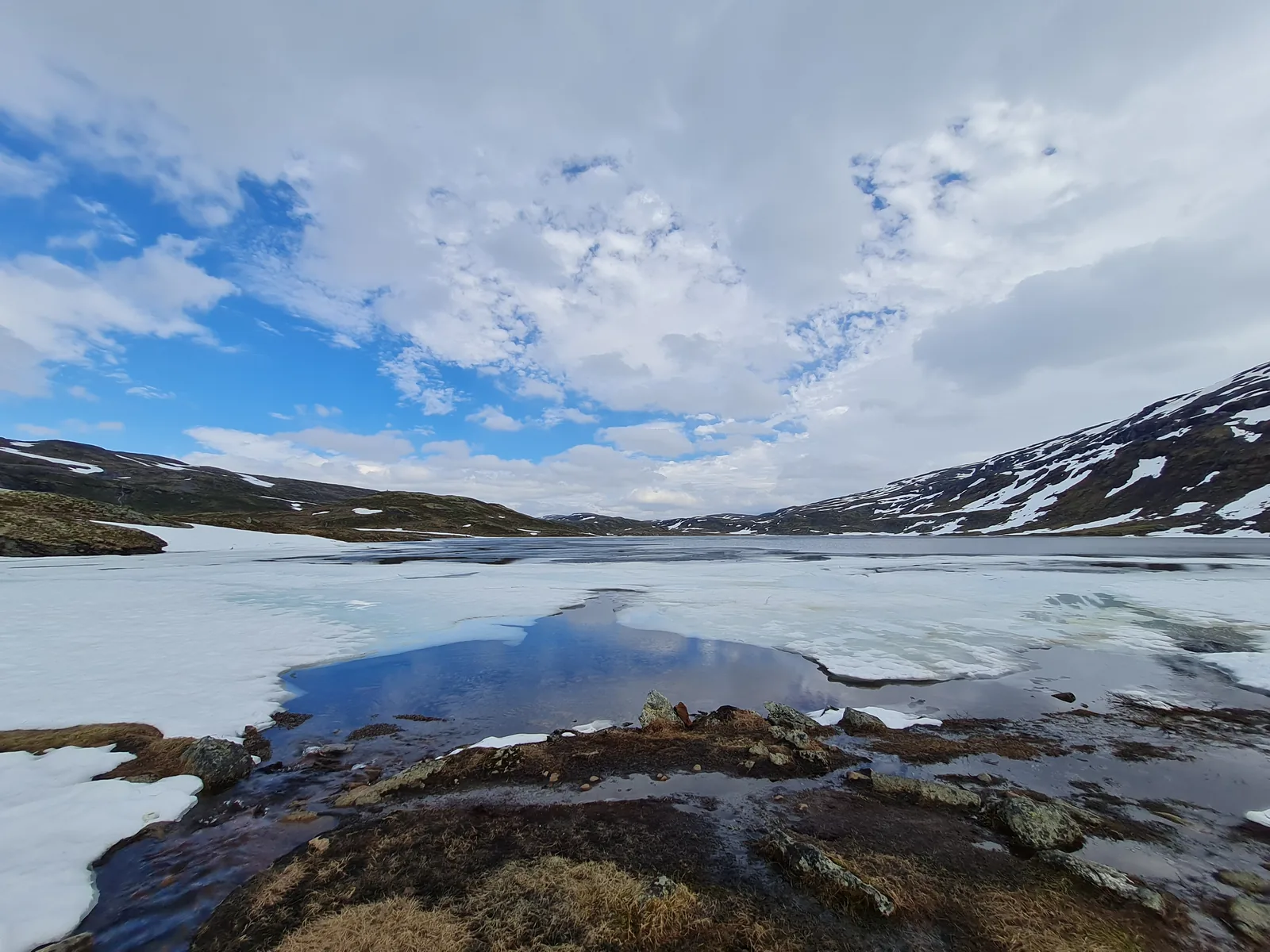 A high alpine tarn with melting pack ice and snowfields on the western Hardangervidda plateau.