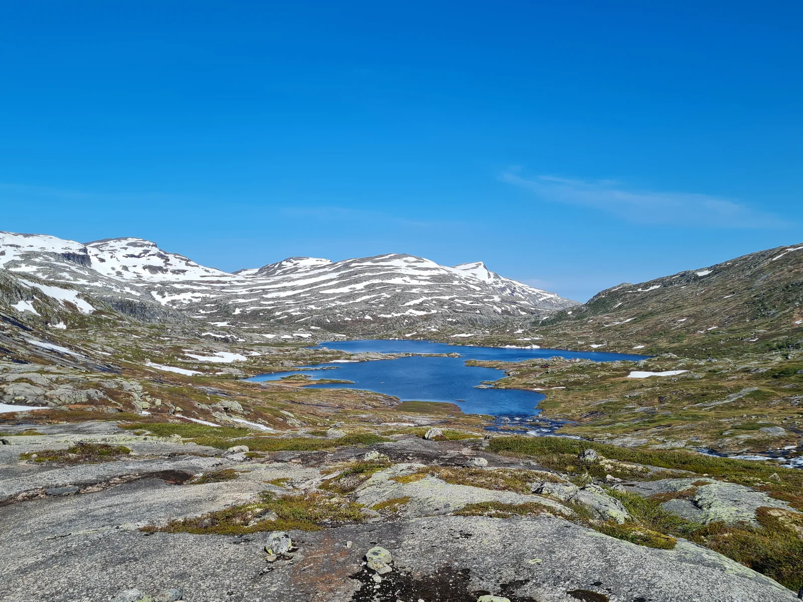 Still morning waters of a mountain tarn mirroring granite shores and distant snowfields on Day 2.