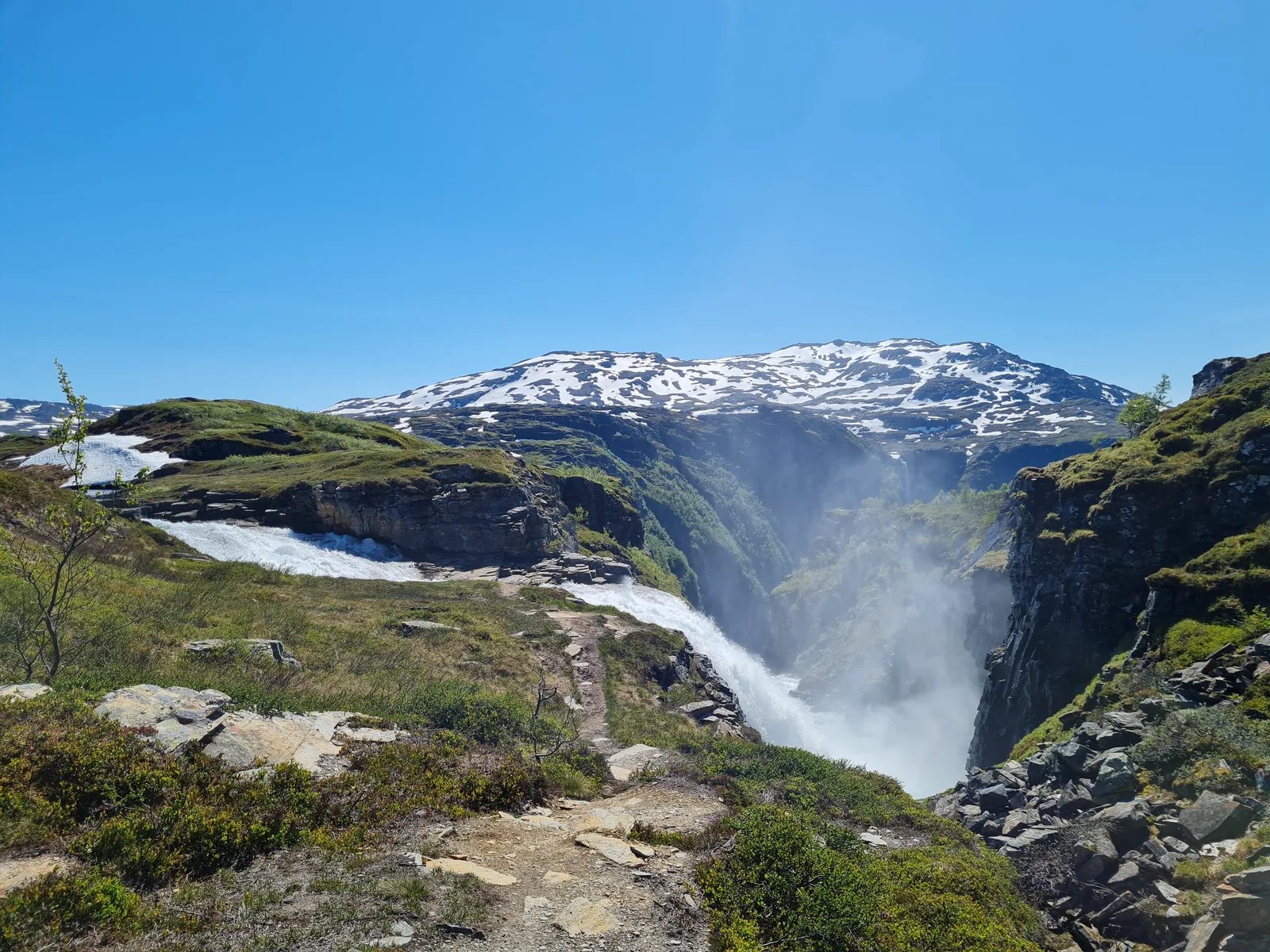 Rushing gorge waterfall carving through the plateau rim with snowy peaks rising in the distance.