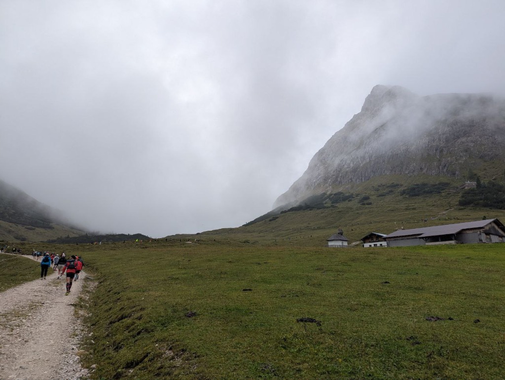 Trail through alpine meadows with a mountain hut and clouds rolling in