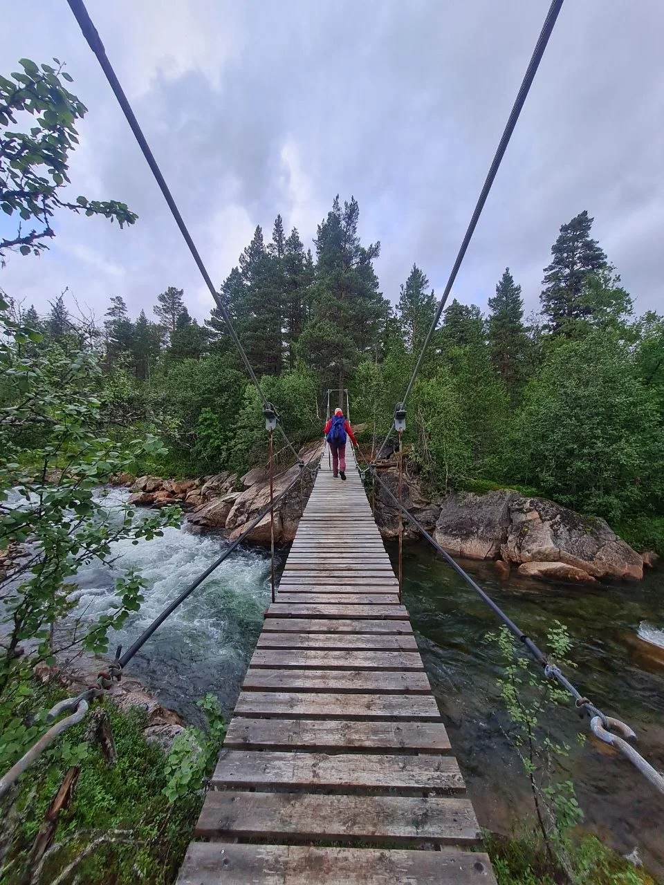 Hiker crossing suspension bridge over river in dense forest