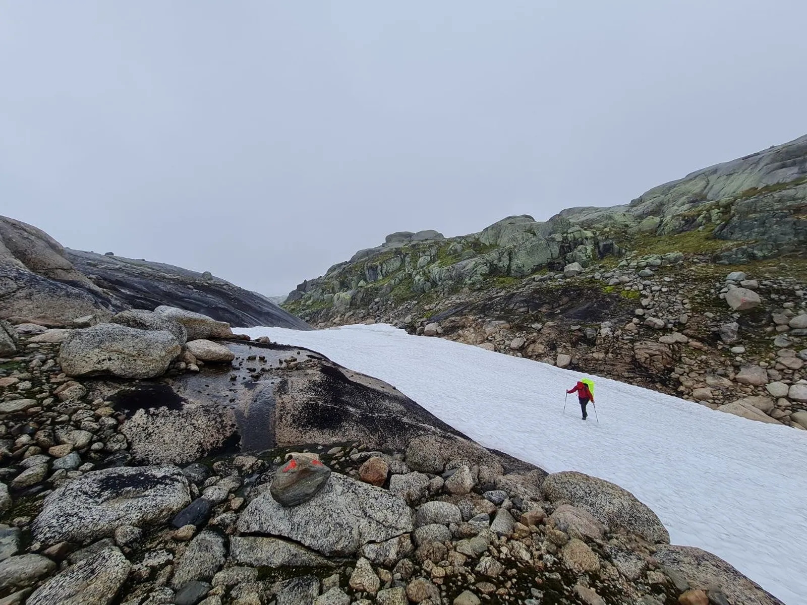 Hiker crosses a snowy mountain pass in rainy southern Norway