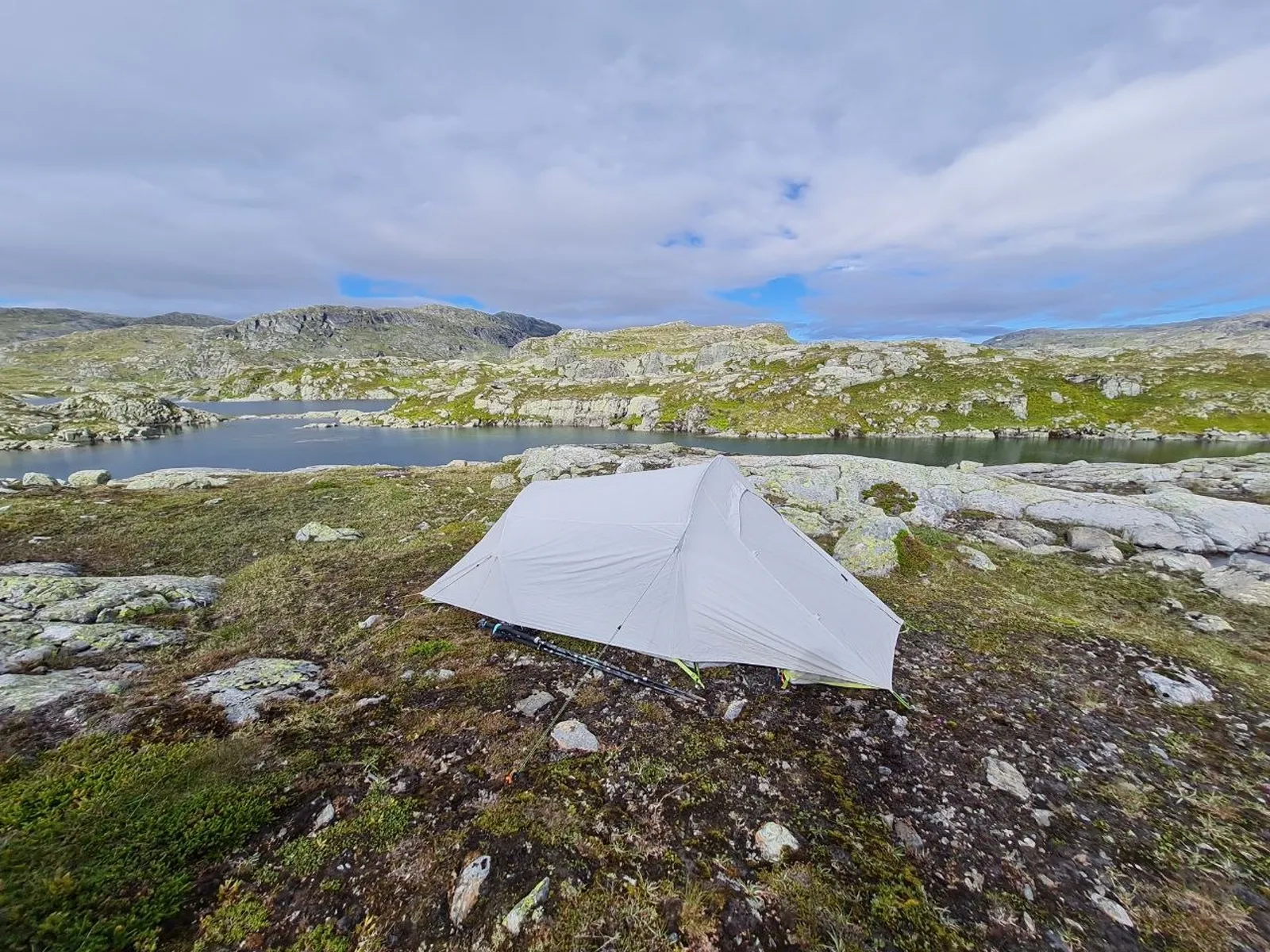 Tent pitched by a serene mountain lake under cloudy skies