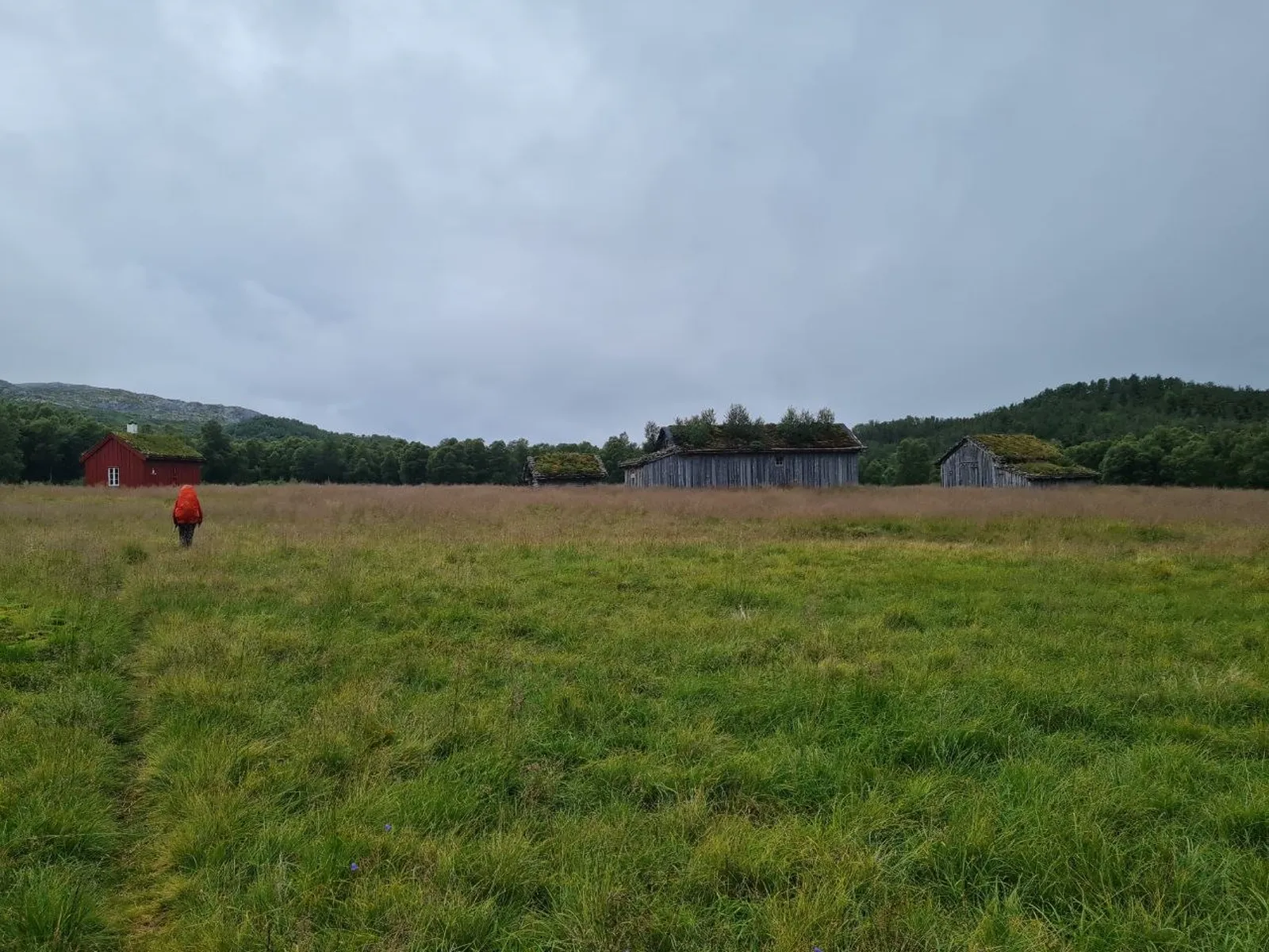 Hiker approaches rustic cabins on a cloudy, wet mountain plateau