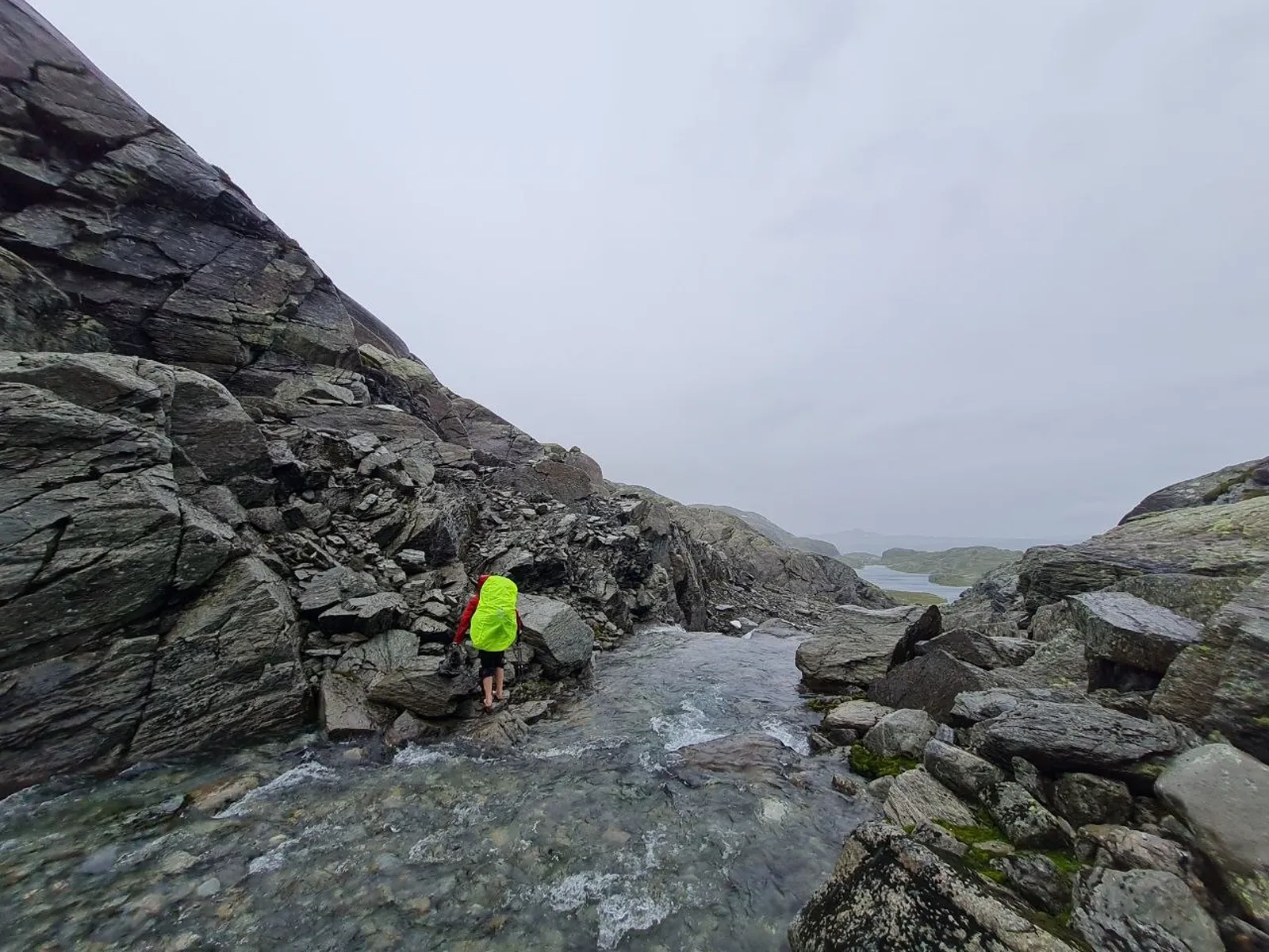 Hiker crosses rocky stream in rugged Ryfylkeheiane mountains under gray skies