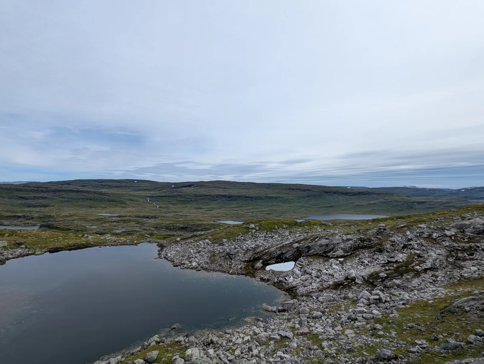 Open fell landscape with tarns, stone cairns, and lingering snowfields at 1,128 m approaching Åsedalen (Day 5).