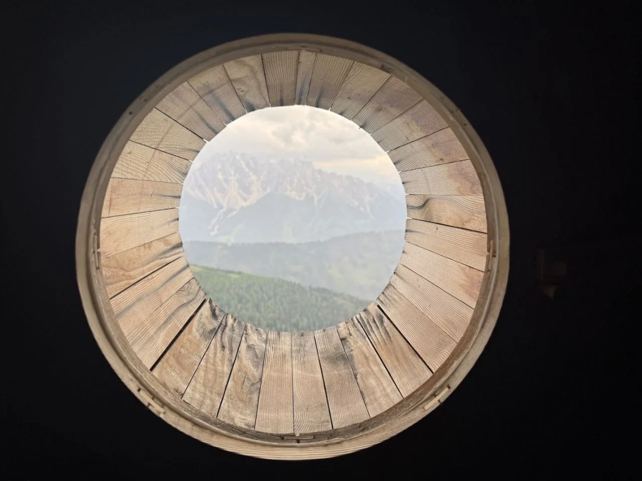 A circular wooden skylight at Bonner Hut frames Dolomite peaks above the valley.