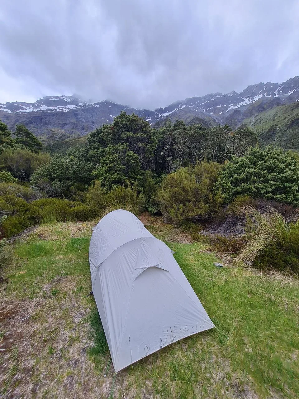 A solo tent pitched on the Rees Dart Track beneath snow-dusted peaks.